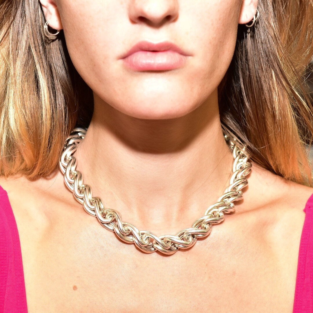 Close-up of a woman's neck and collar area wearing a chunky silver chain link necklace against a bright pink top.