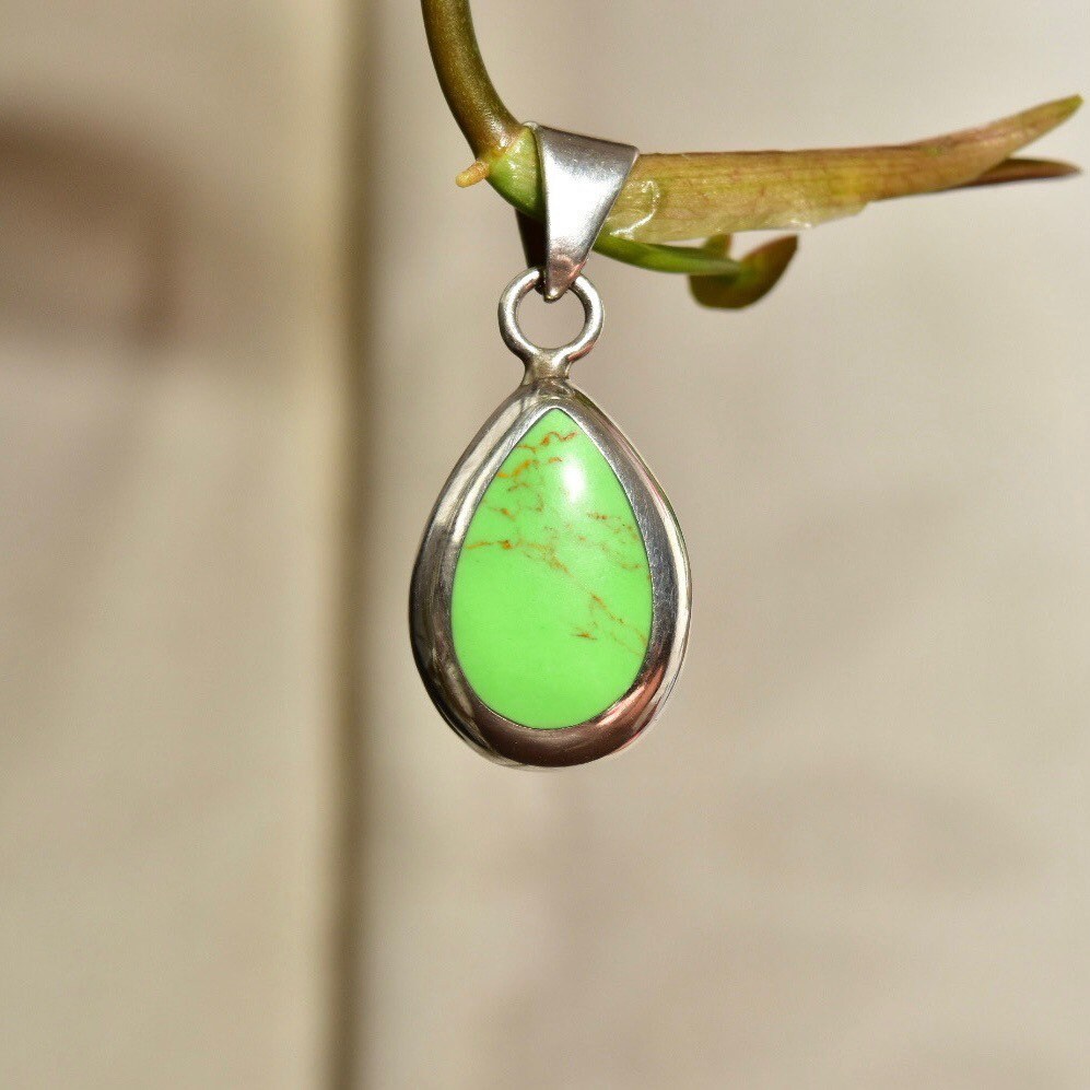 Vintage Mexican sterling silver teardrop pendant with lime green gaspeite gemstone in polished silver drop setting hanging from branch