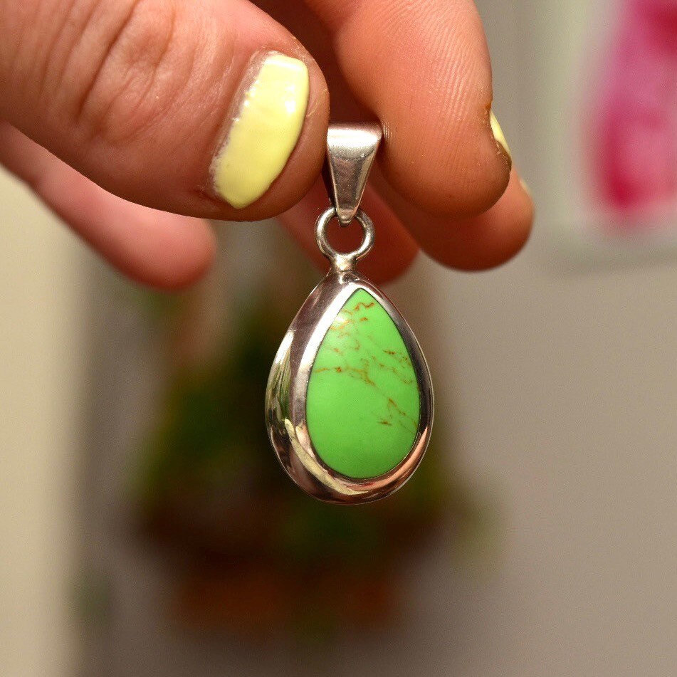 Vintage Mexican sterling silver teardrop pendant featuring a lime green gaspeite gemstone in a polished silver setting, held between fingers to show scale and detail.