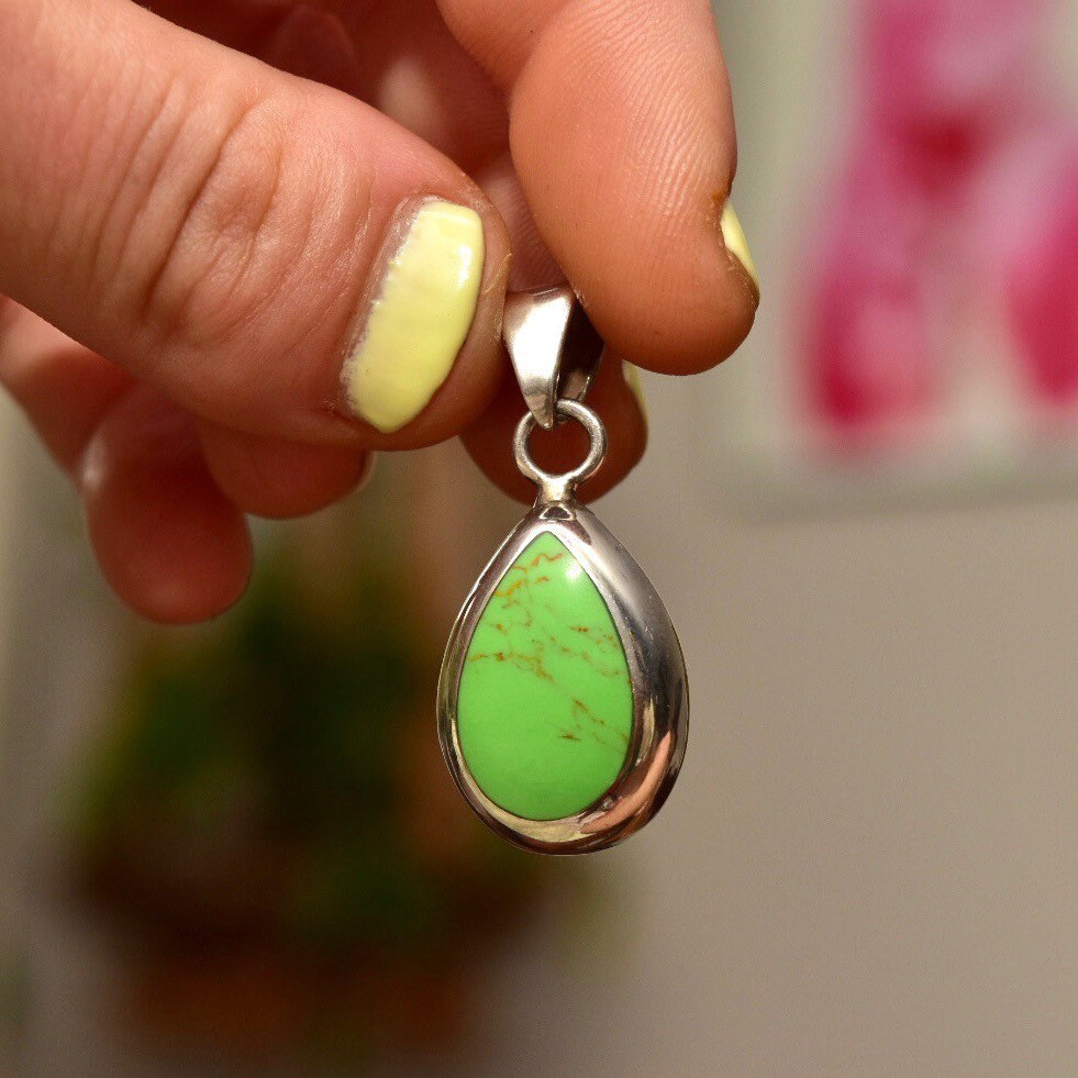 Vintage Mexican sterling silver teardrop pendant featuring a lime green gaspeite gemstone in a polished silver setting, held between fingers to show scale and detail.