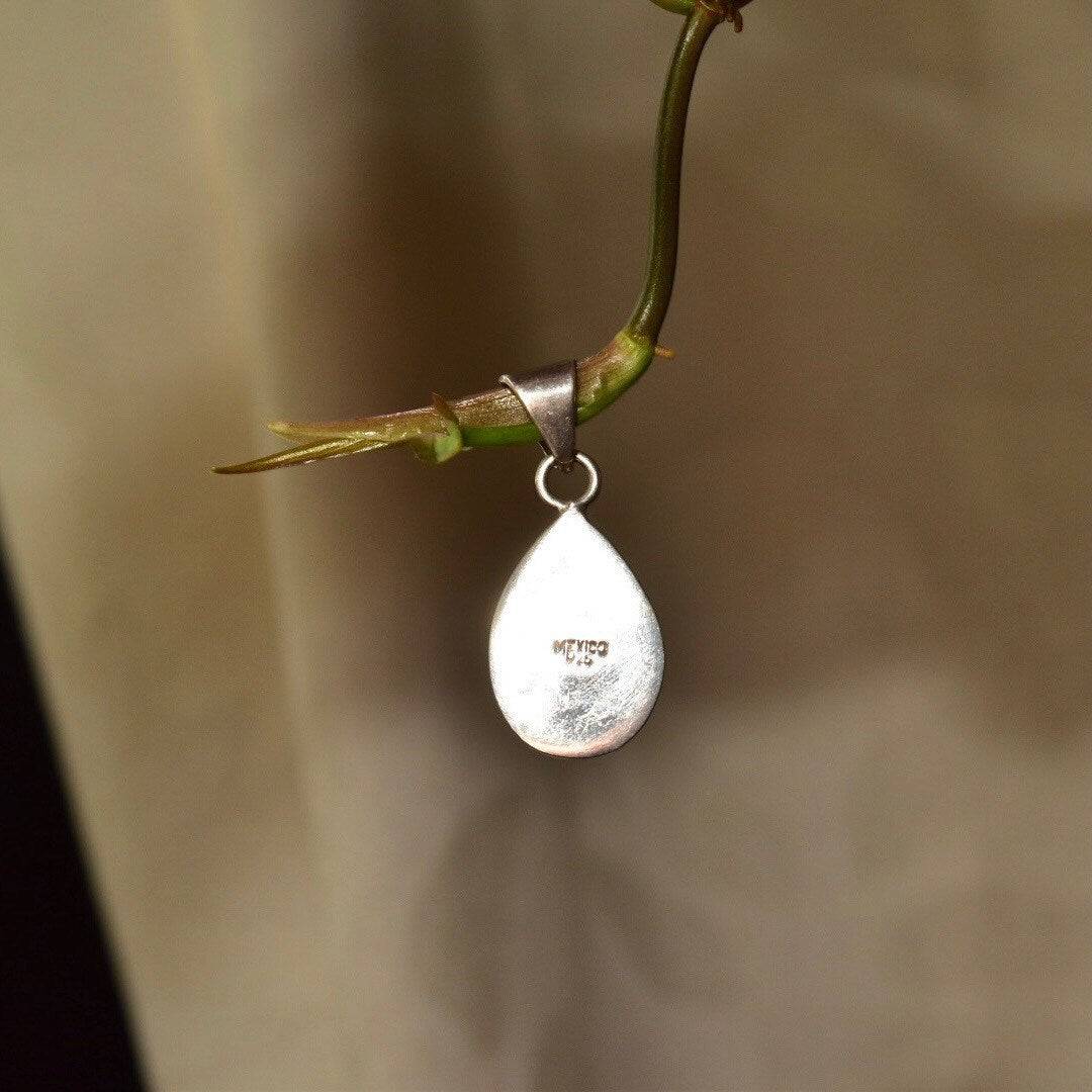 Vintage Mexican sterling silver teardrop pendant with lime green gaspeite gemstone set in polished silver drop setting hanging from thin stem, photographed in soft focus brown background.