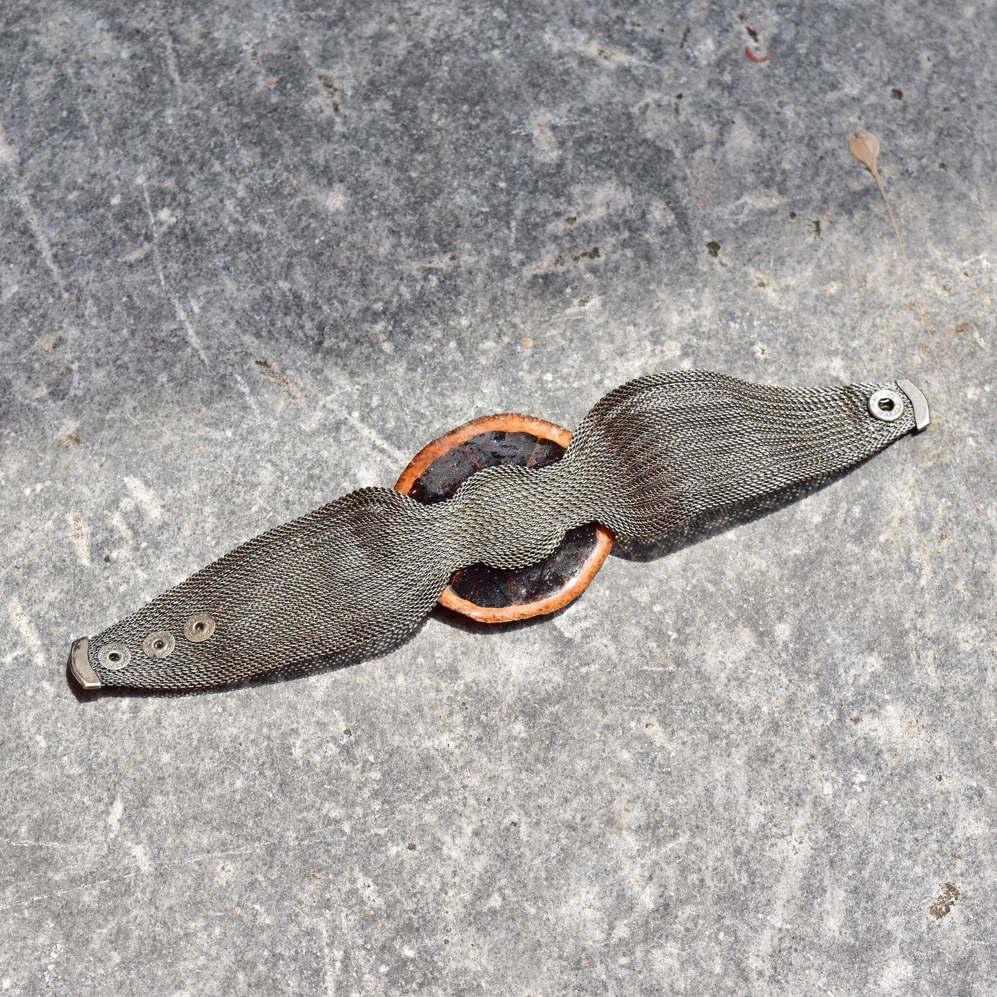 Preserved orange slice cuff bracelet with silver mesh band and iridescent purple glaze on gray background