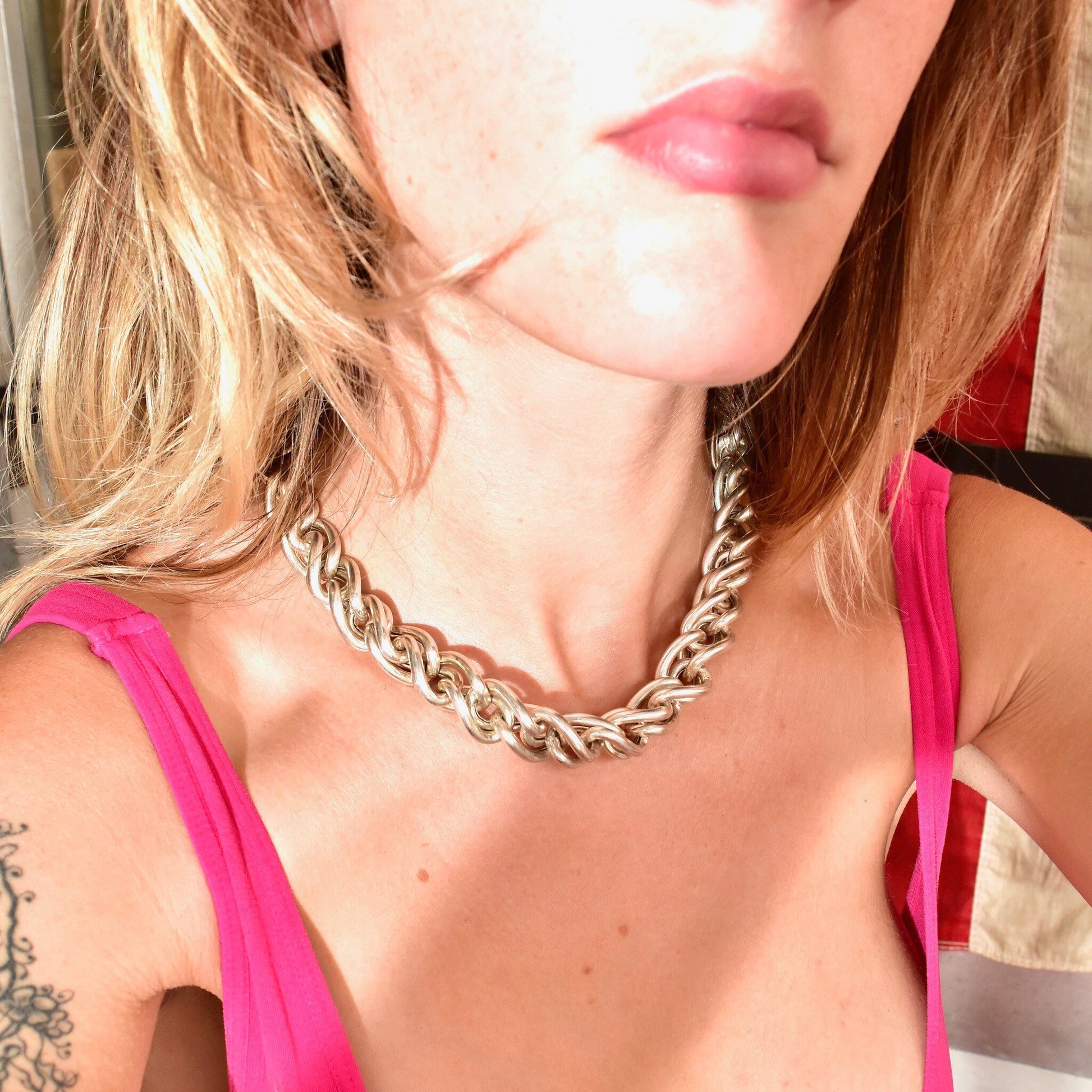 Close-up photo of a woman wearing a chunky sterling silver chain link choker necklace in a puffed Singapore or twisted rope style, made in Italy. The necklace makes a bold modernist statement against her pink top.