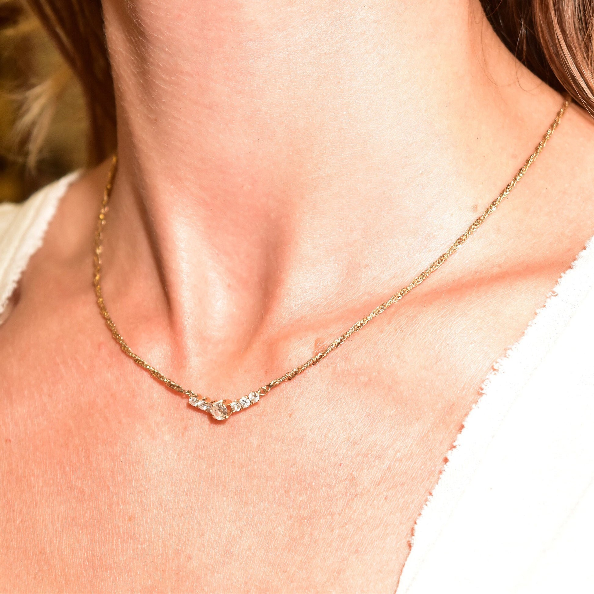 Gold diamond bar necklace on woman's chest and neck, showcasing the delicate chain and sparkling diamond pendant against her skin.