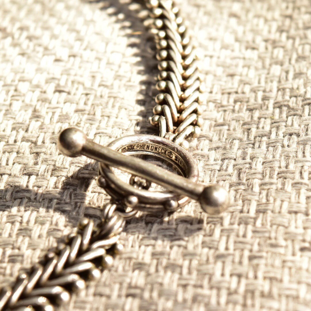 Sterling silver foxtail toggle chain necklace on textured fabric background, showing intricate chain links and toggle clasp closure, 17 inches long.