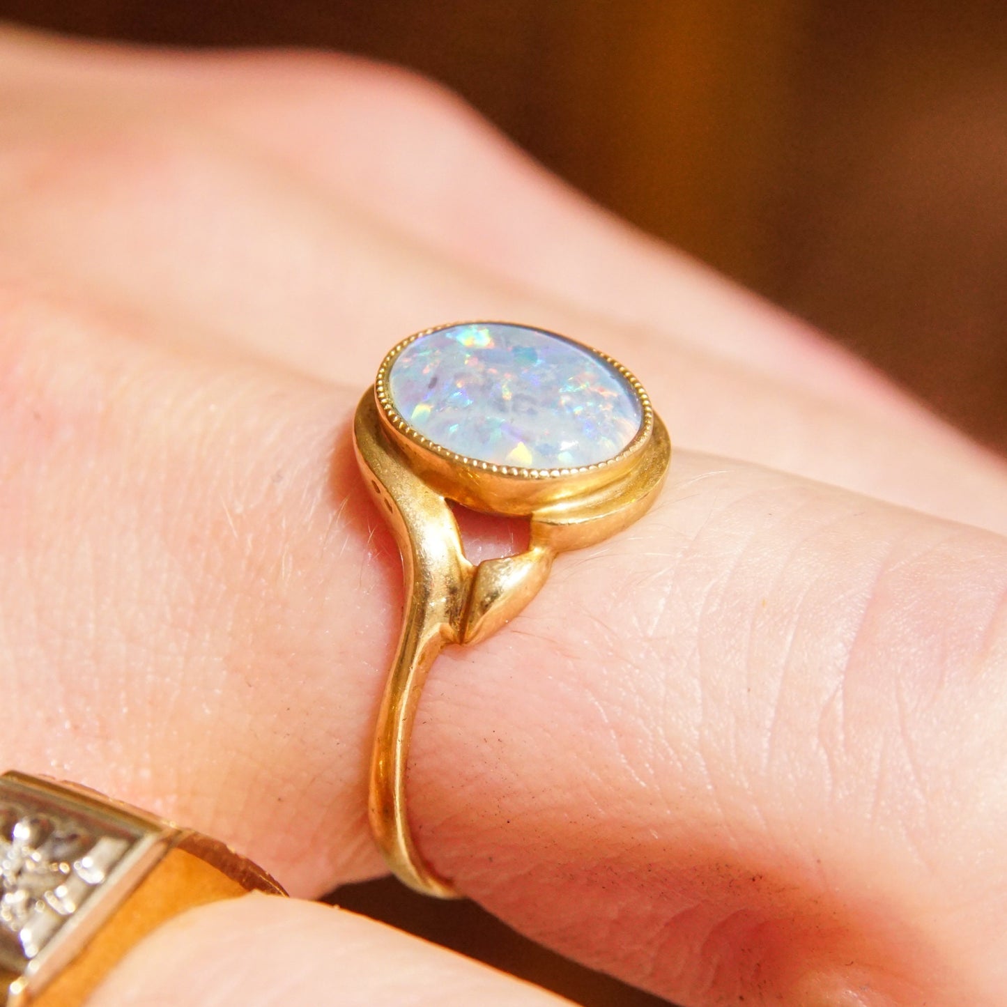 10K yellow gold cocktail ring featuring a round opal triplet gemstone, worn on a finger to showcase the iridescent play-of-color. Estate jewelry piece and October birthstone ring in a size 8 1/4 US.