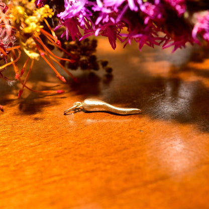 14K yellow gold Italian horn charm pendant on wooden surface with purple flowers, small vintage brushed gold cornicello good luck charm approximately 26mm in size