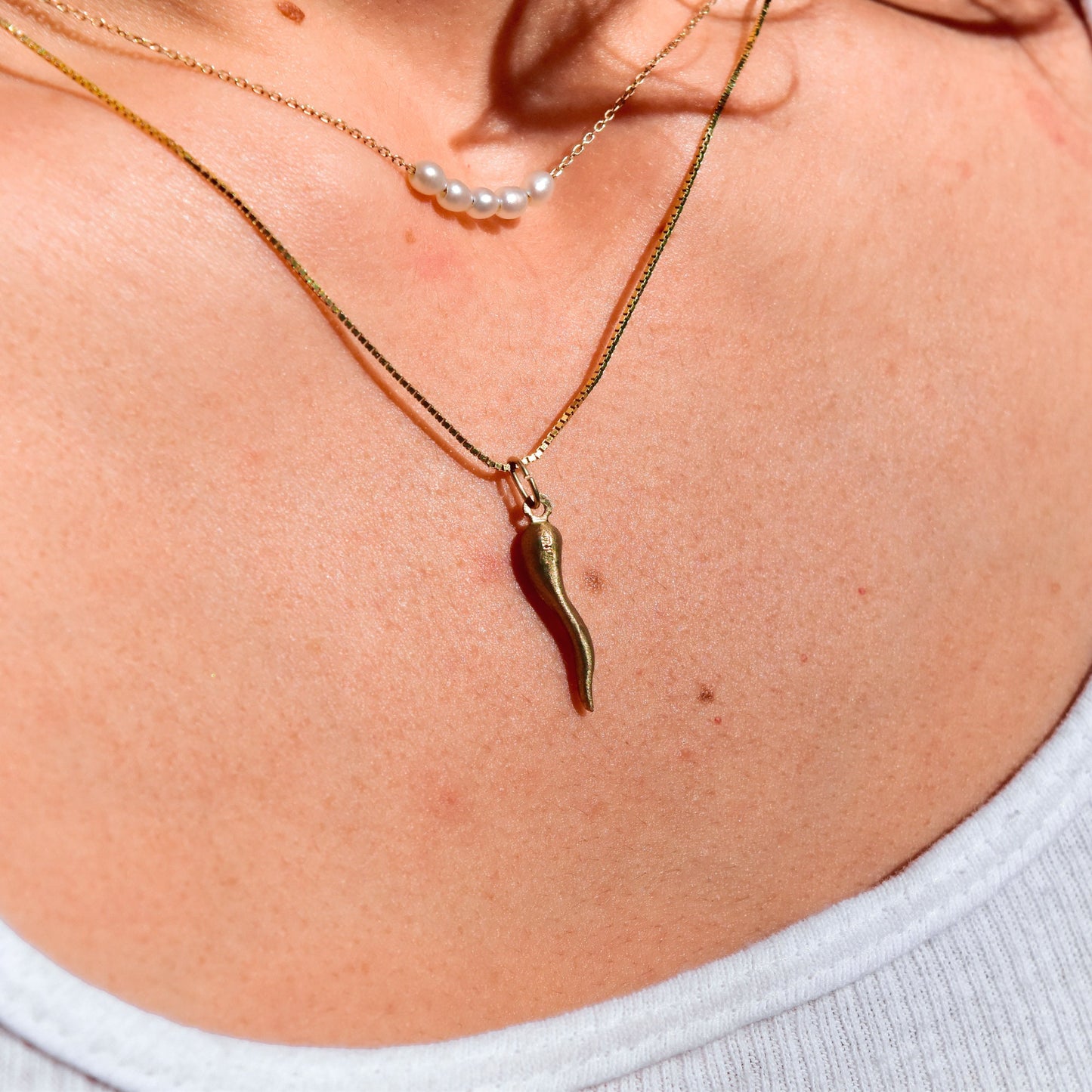 Delicate golden necklaces with pearls and a small horn-shaped pendant resting on the collarbones of a person, symbolizing good luck and protection in Italian tradition.