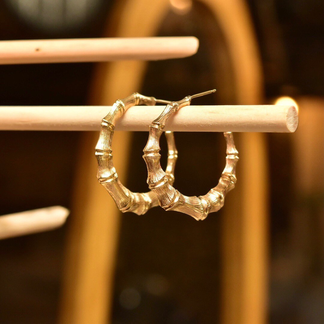 14K yellow gold bamboo hoop earrings hanging on a wooden display rack, showing the intricate wrapped design of the vintage statement jewelry studs.