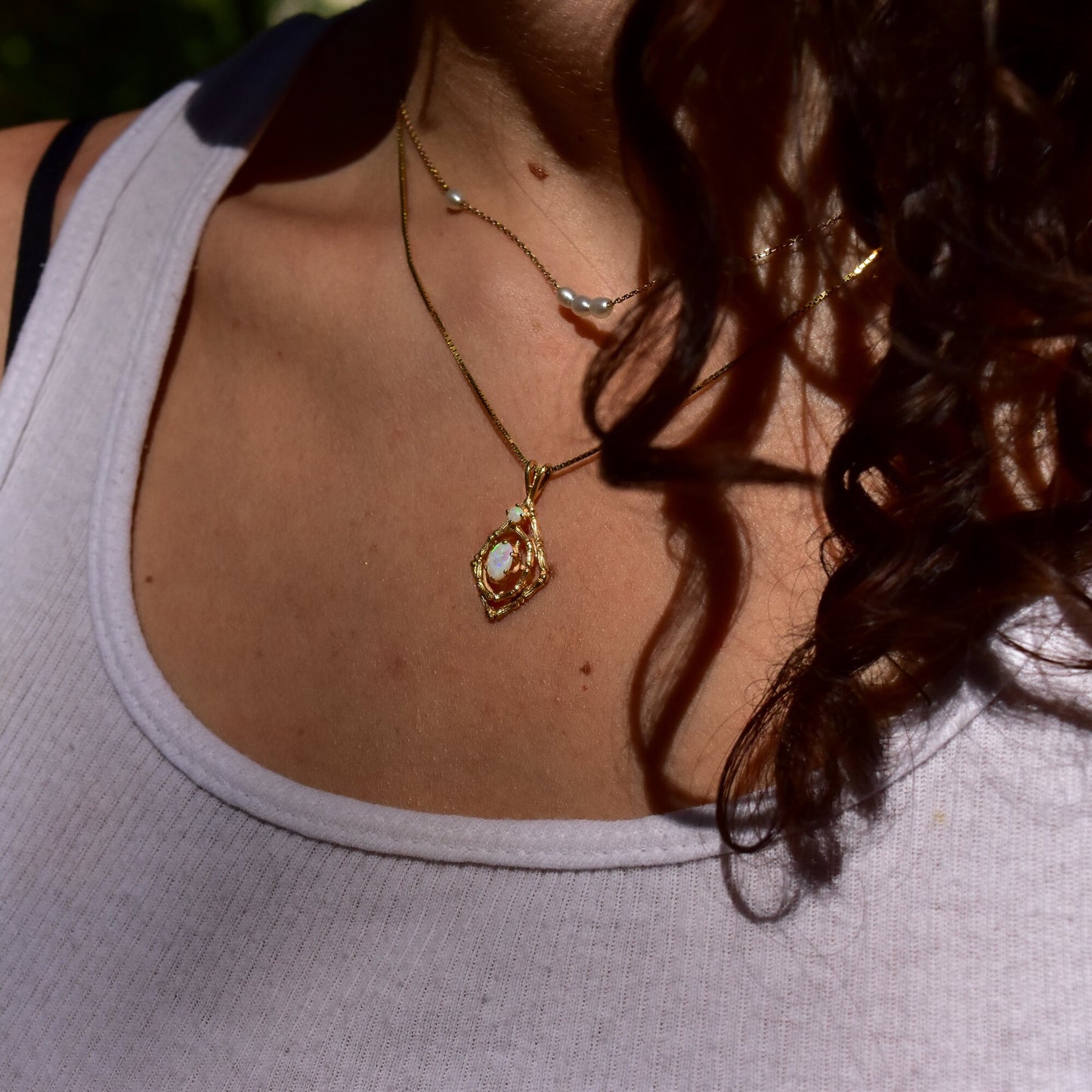 10K yellow gold opal pendant necklace with bamboo motif design worn by a woman with curly brown hair against her shoulder and white top.