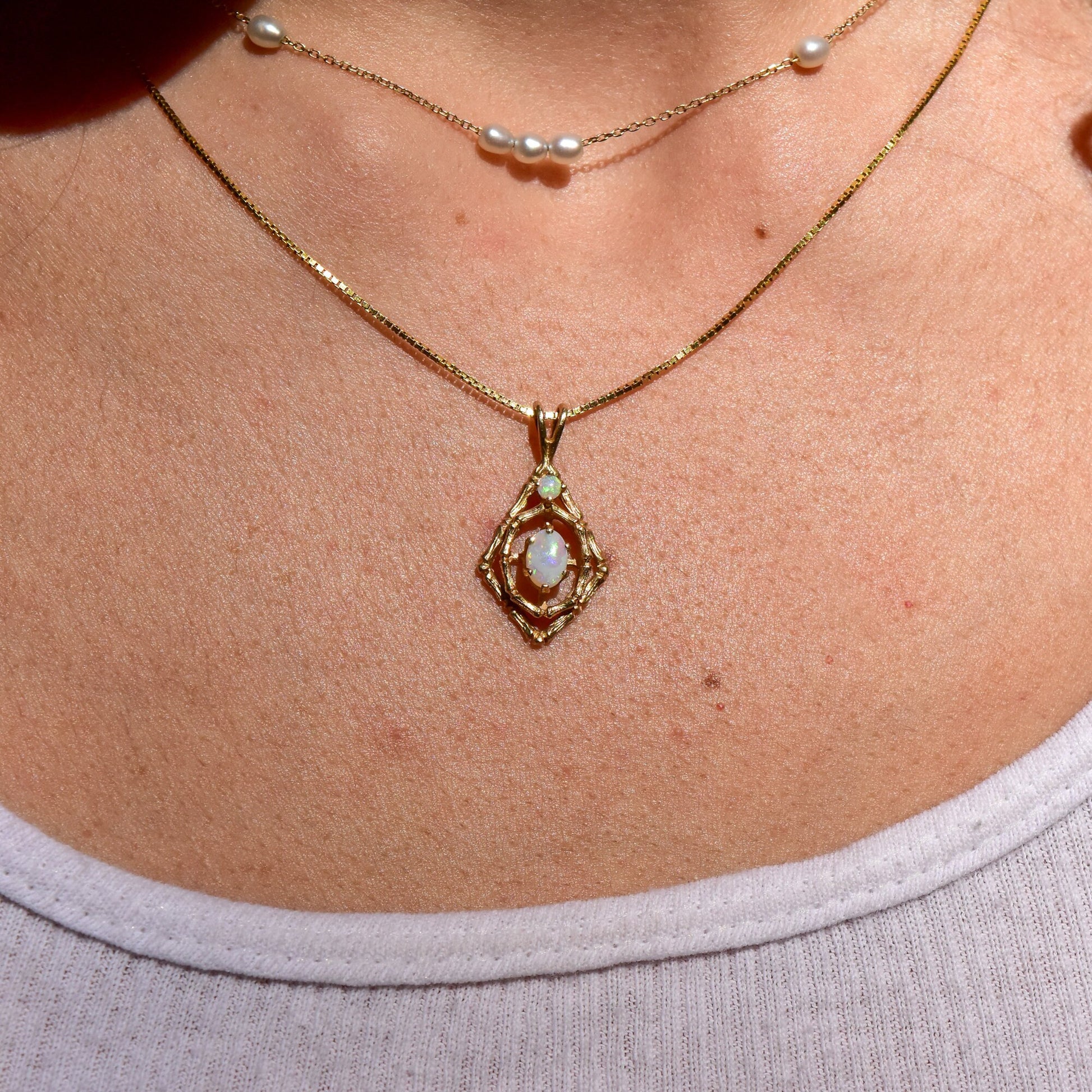 10K yellow gold pendant necklace featuring two white opal cabochon stones in an intricate bamboo-inspired design, displayed on a woman's neck against her skin.
