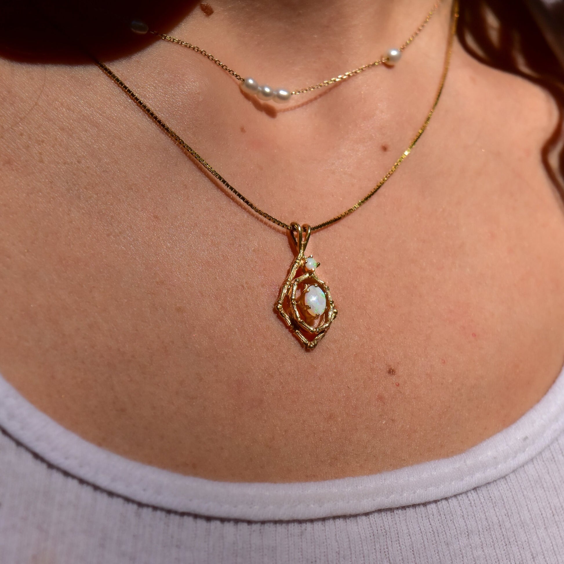 10K yellow gold vintage estate pendant necklace featuring two oval white opal cabochons accented by bamboo motif, hung from delicate gold chain, shown on model's neck against skin