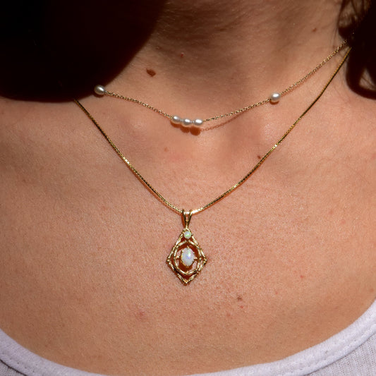 10K yellow gold opal pendant necklace with bamboo motif, featuring two white opal cabochon gemstones, shown worn on a model's neck against bare skin.