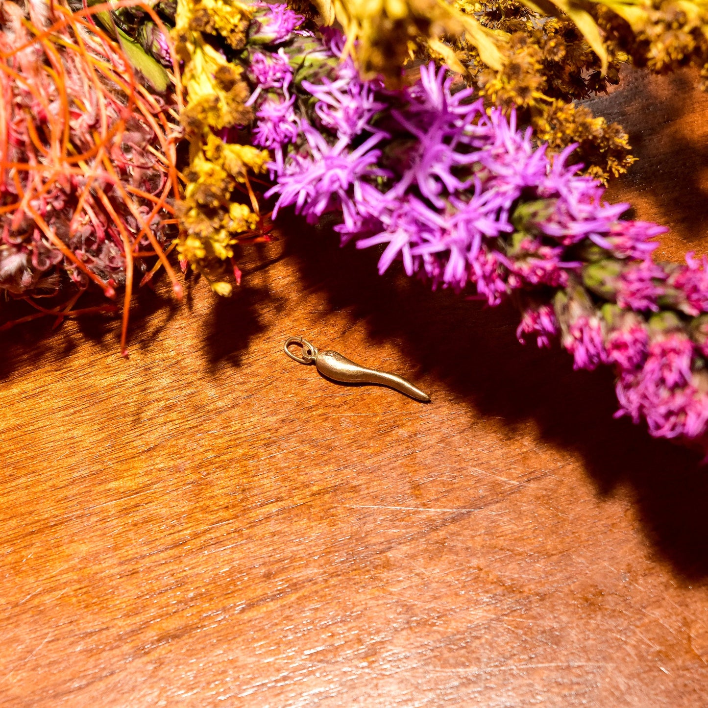 Brushed yellow gold Italian horn charm on wooden surface with purple floral arrangement