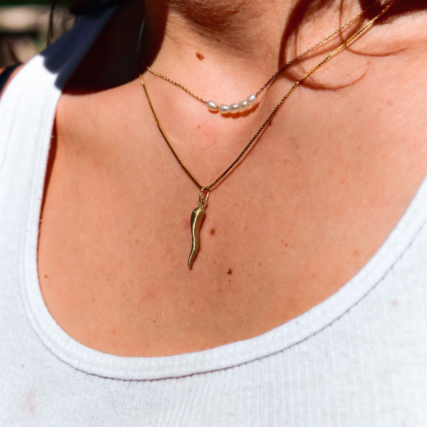14K brushed yellow gold Italian horn charm necklace worn on a woman's neck, showing a cute mini puffed cornicello pendant - a vintage good luck charm measuring 26mm in size.