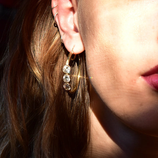 14K yellow gold hoop earrings with three dangling cubic zirconia stones, worn on a woman's ear with brown hair