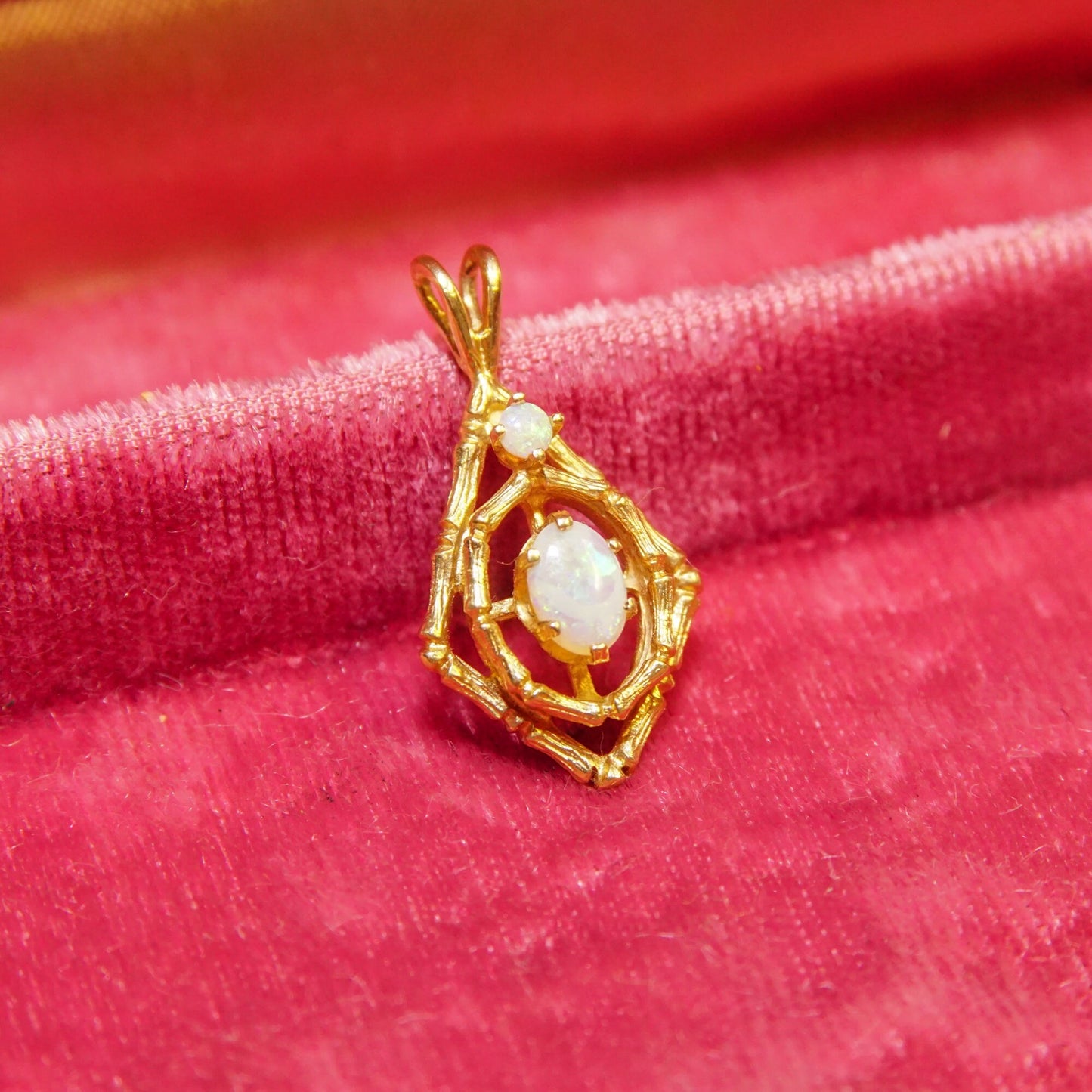 10K yellow gold bamboo motif opal pendant with two white opal cabochon stones on red velvet fabric