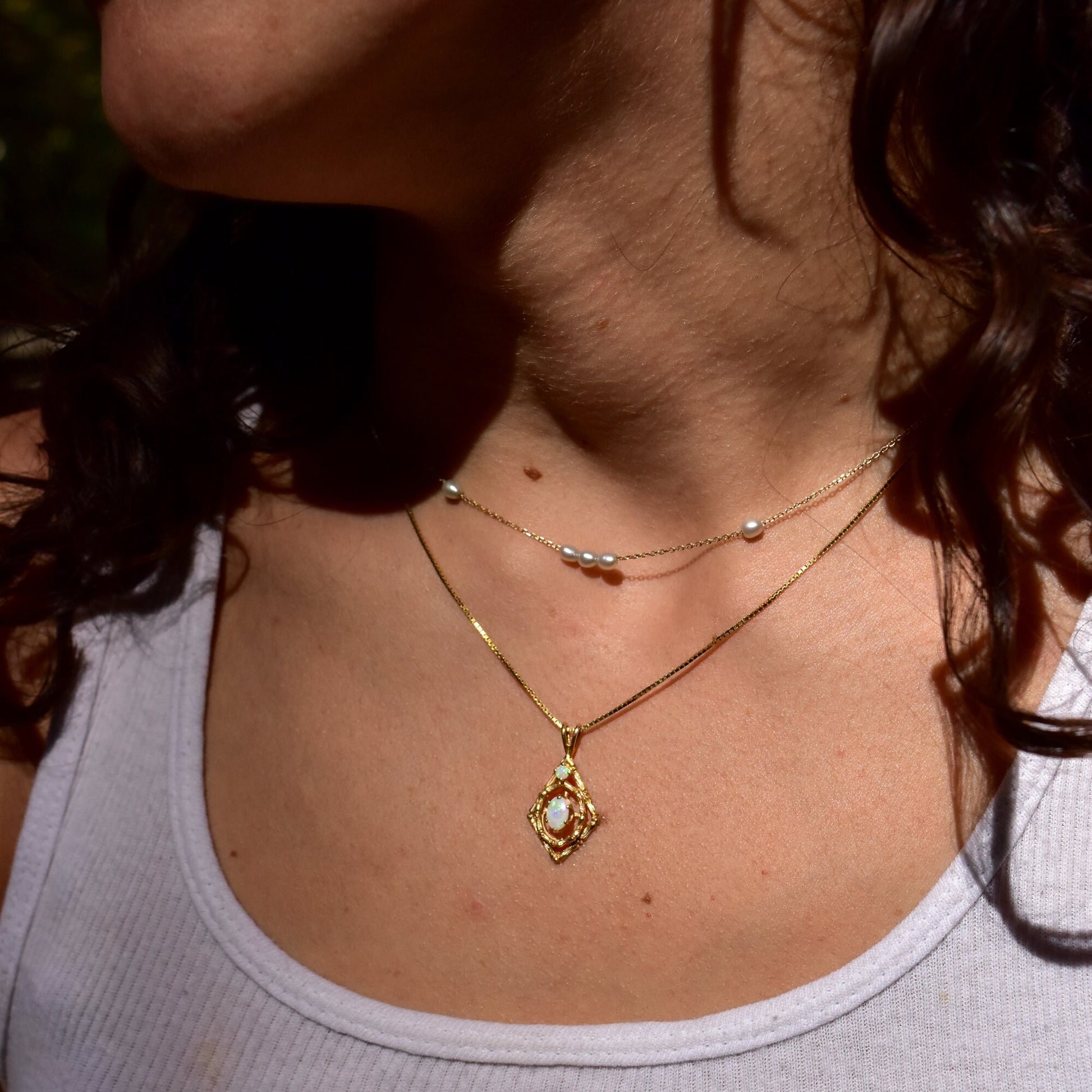 10K yellow gold opal pendant necklace with bamboo motif and two white opal cabochon stones, worn by a person with curly brown hair, cropped image showing neck and upper chest.