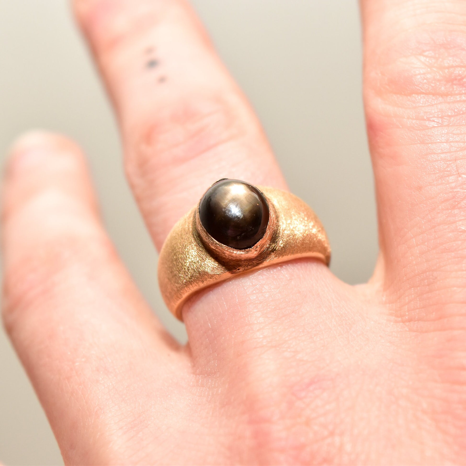 14K yellow gold men's pinky ring featuring a round black star sapphire cabochon with asterism, displayed on a hand, estate jewelry size 8 3/4 US.