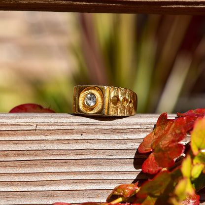 Vintage gold signet ring with diamond accents and textured geometric design, displayed on weathered wooden surface with red autumn leaves.