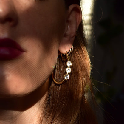 14K yellow gold three-stone cubic zirconia hoop earrings worn on a woman's ear, with long brown hair partially visible