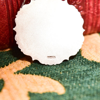 White scrimshaw flower pendant with sterling silver repousse setting on green and orange textured background