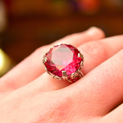 10K white gold pink ruby cocktail ring with ornate filigree setting, featuring a large synthetic ruby gemstone, in an Art Deco style. Ring size is 6 3/4 US, shown on a person's hand.