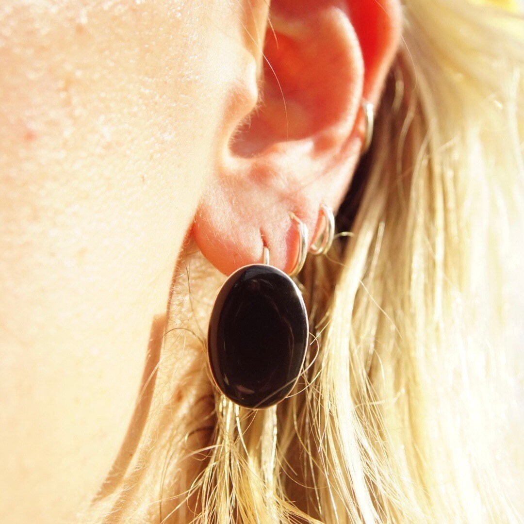 Close up of a woman's ear wearing a black onyx gemstone earring set in sterling silver with a dangle design, the earring is approximately 1 inch long against blonde hair