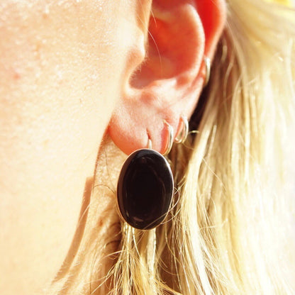 Close up of a woman's ear wearing a black onyx gemstone earring set in sterling silver with a dangle design, the earring is approximately 1 inch long against blonde hair