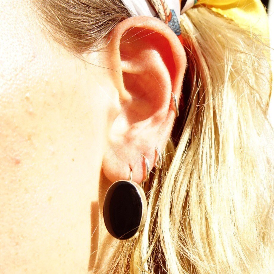 Close-up view of a woman's ear with blonde hair wearing a black onyx dangle earring surrounded by hair strands, giving an artistic vintage aesthetic.