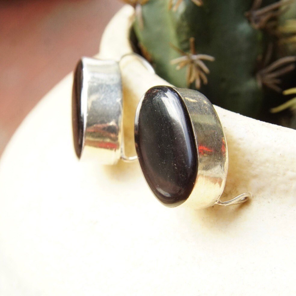 Vintage modernist sterling silver and black onyx drop earrings from Taxco, Mexico. The oval-shaped onyx stones are set in polished silver bezels suspended from silver latch hook ear wires. The dangle earrings measure approximately 1 inch long.