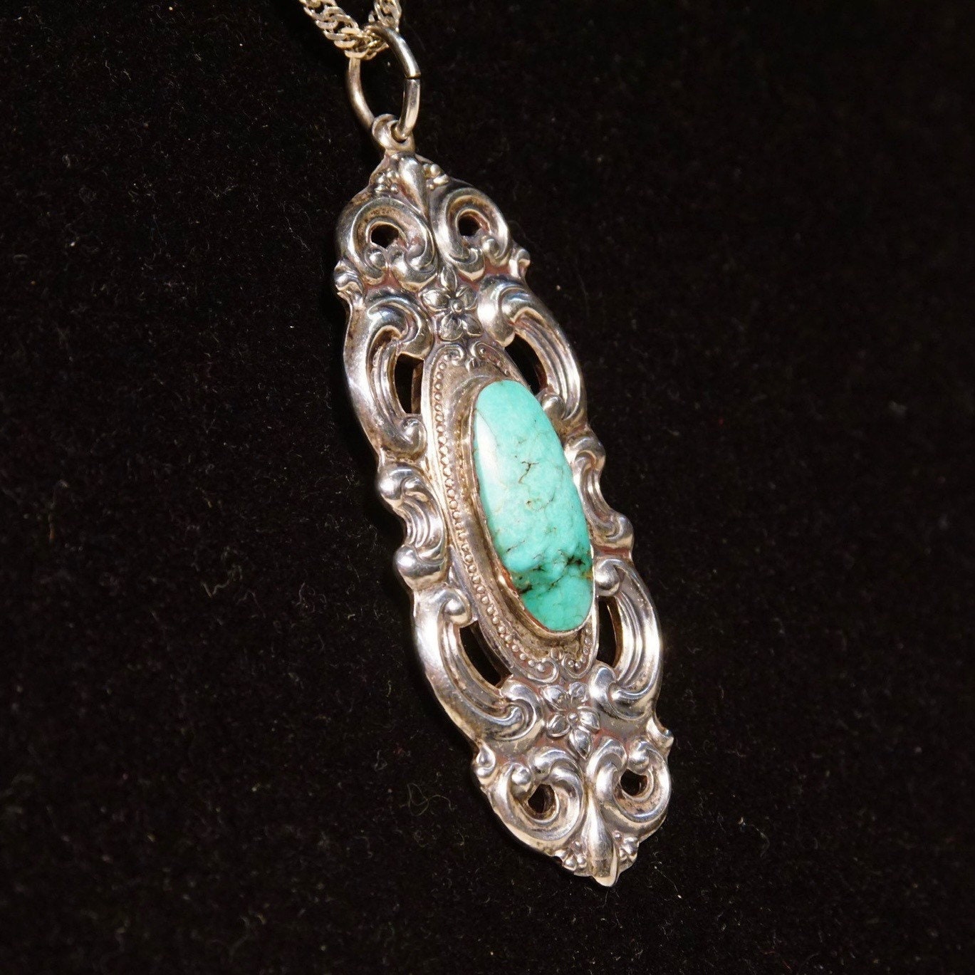 Vintage Towle sterling silver pendant featuring an ornate embossed repousse design with floral motifs in an Art Nouveau style, set with a turquoise cabochon. The pendant measures 2 3/4 inches in length.