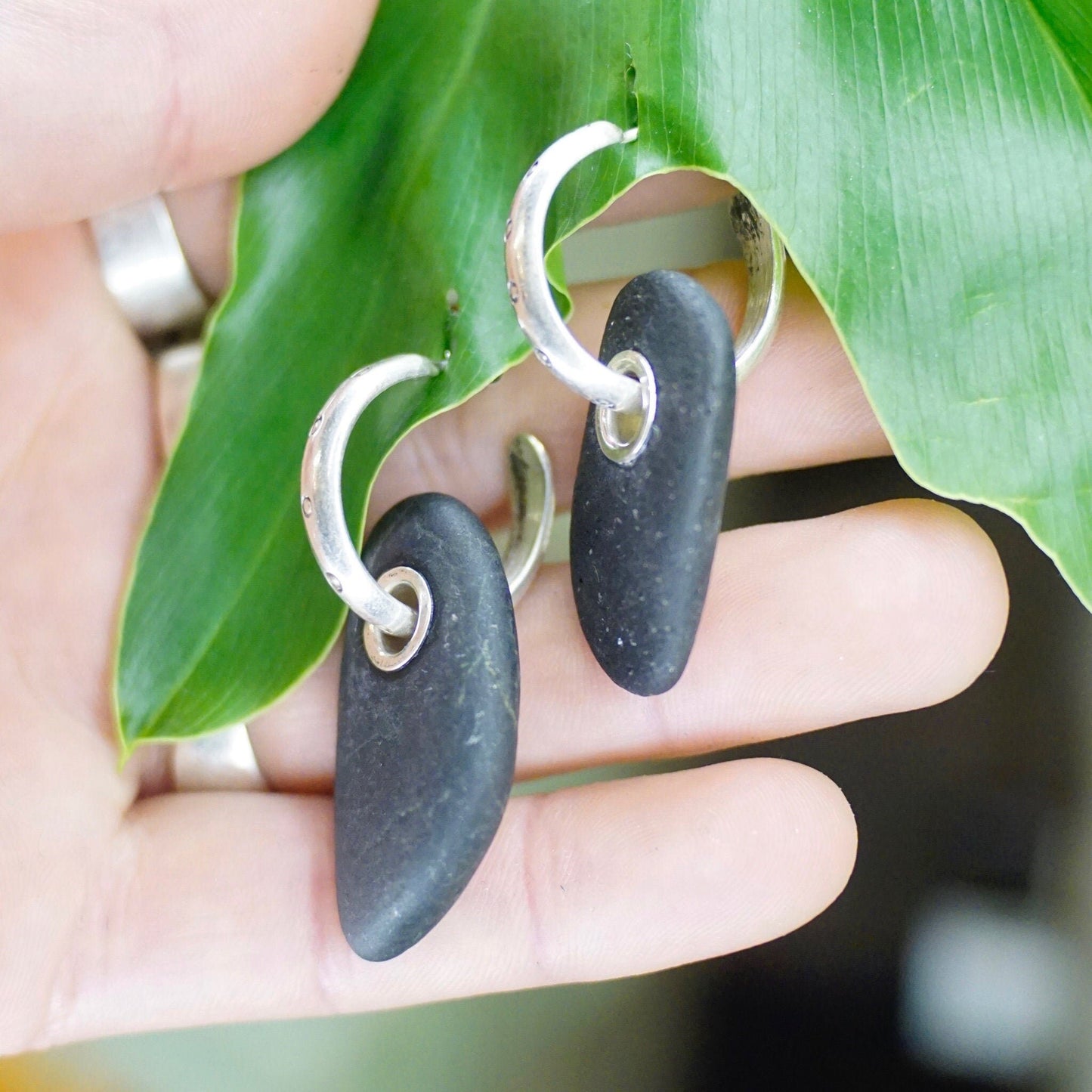 Vintage sterling silver hoop earrings with black stone charms, small stud hoops featuring threaded rock pendants on tropical green leaf, artisan handmade 925 silver statement jewelry closeup