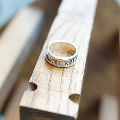 Vintage Tiffany & Co. 1995 Sterling Silver Atlas Roman Numeral Ring on weathered wooden plank, petite silver band ring with embossed numeral design, 925 Italy hallmark, size 6 US.