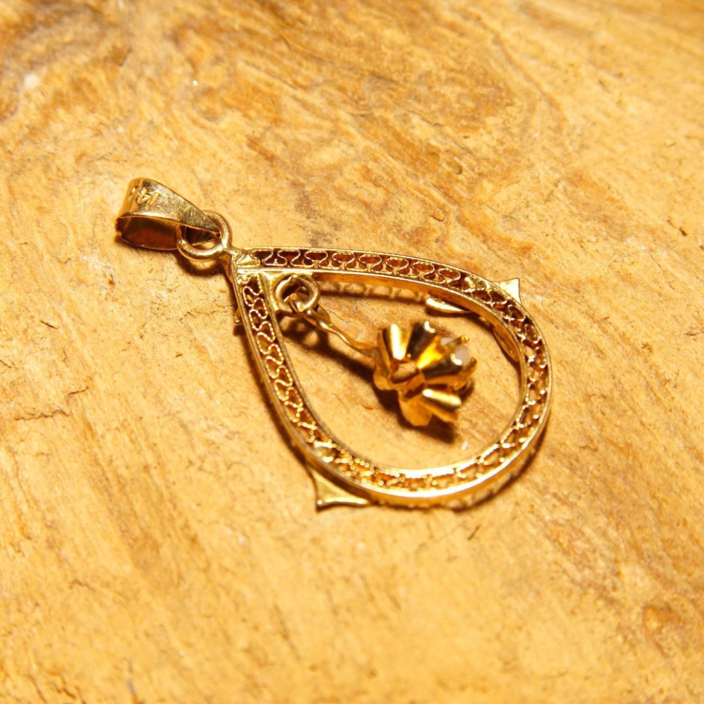 Antique 14K gold filigree teardrop pendant with seed pearl, prong-set flower dangle, and engraved leaf details on a textured gold background.