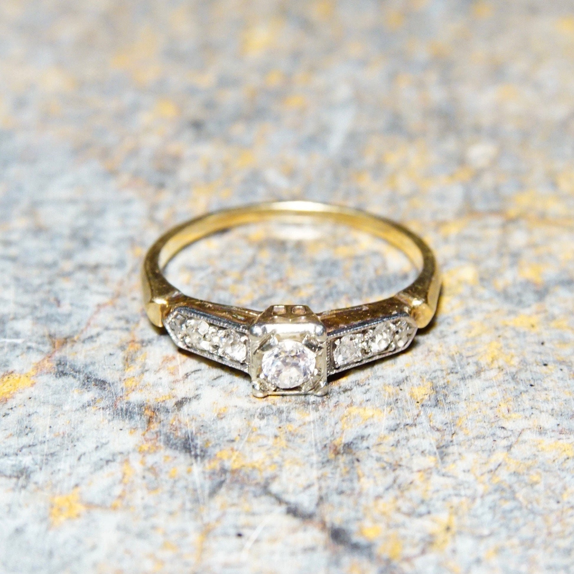 Vintage 14K & 18K gold diamond engagement ring with yellow gold band, white gold settings, and .14 carat old European cut center stone on textured gray background