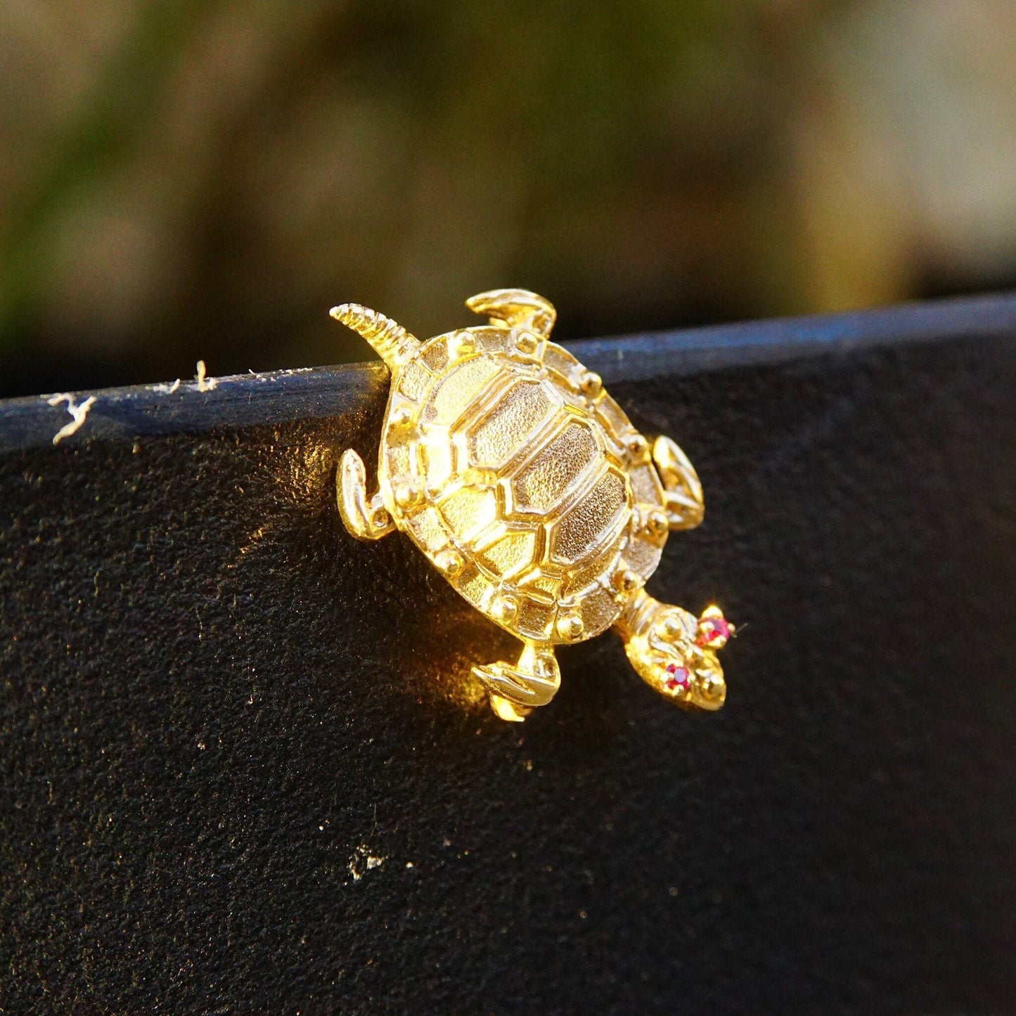 Vintage 14K yellow gold turtle brooch pin with ruby gemstone eyes, depicting a cute turtle-shaped animal jewelry piece in a close-up view on a dark textured surface.