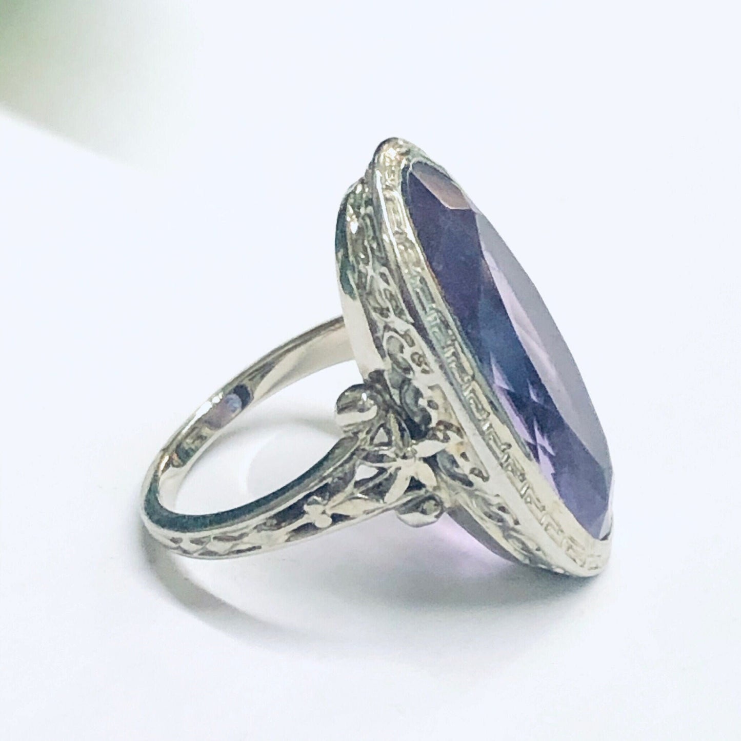 Vintage 18K white gold ring featuring an oval-cut amethyst gemstone accented by intricate floral engravings along the band, creating an elegant and timeless piece of fine jewelry suitable for an engagement or special occasion.