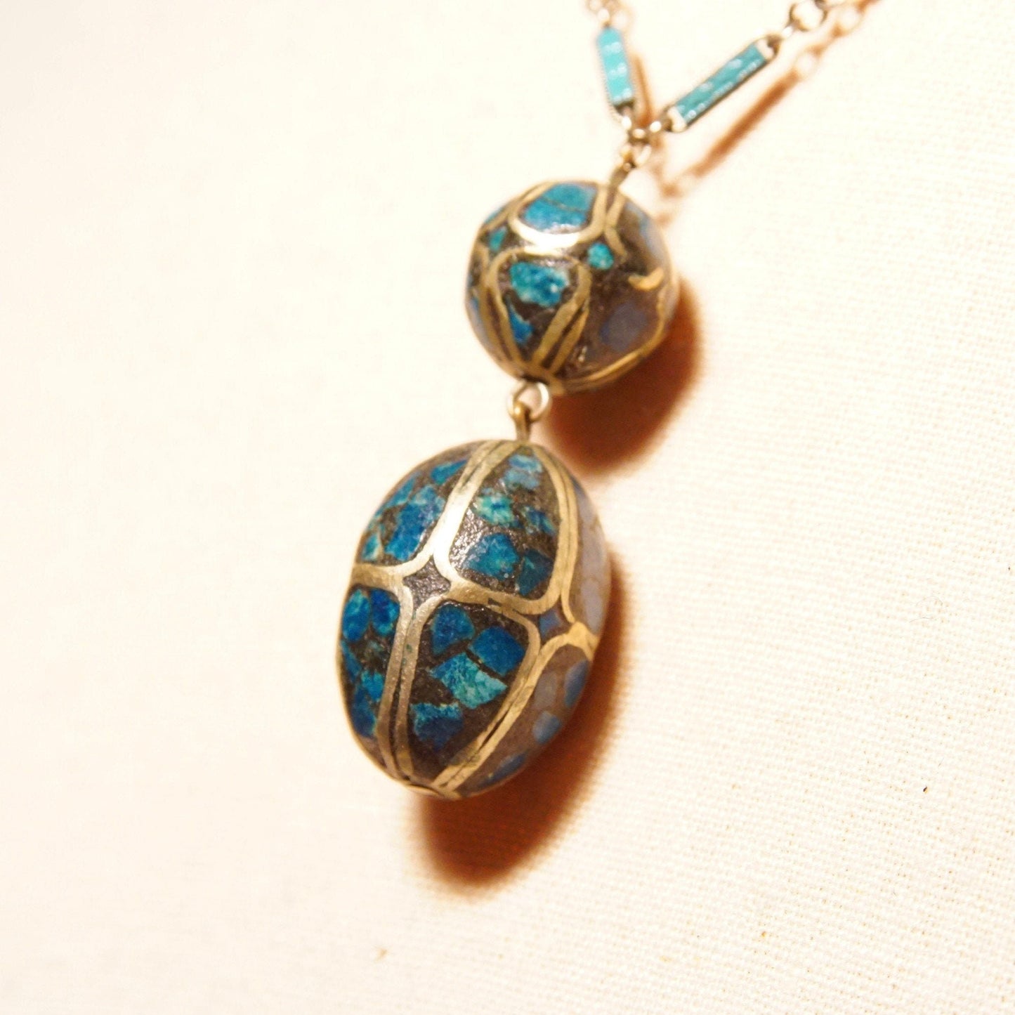 Vintage Indian mosaic turquoise and brass inlay bauble pendant necklace with two oval beads featuring blue enamel inlay in an intricate pattern, suspended from a delicate silver link chain measuring 18 inches in length.