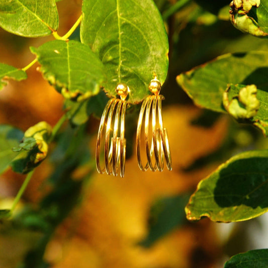 Vintage minimalist 14K gold wire hoop earrings with four-strand design and cuff accents featuring a gold bead, hallmarked 14K POM, measuring approximately 1 1/8 inches in length, displayed on a lush green leafy background.