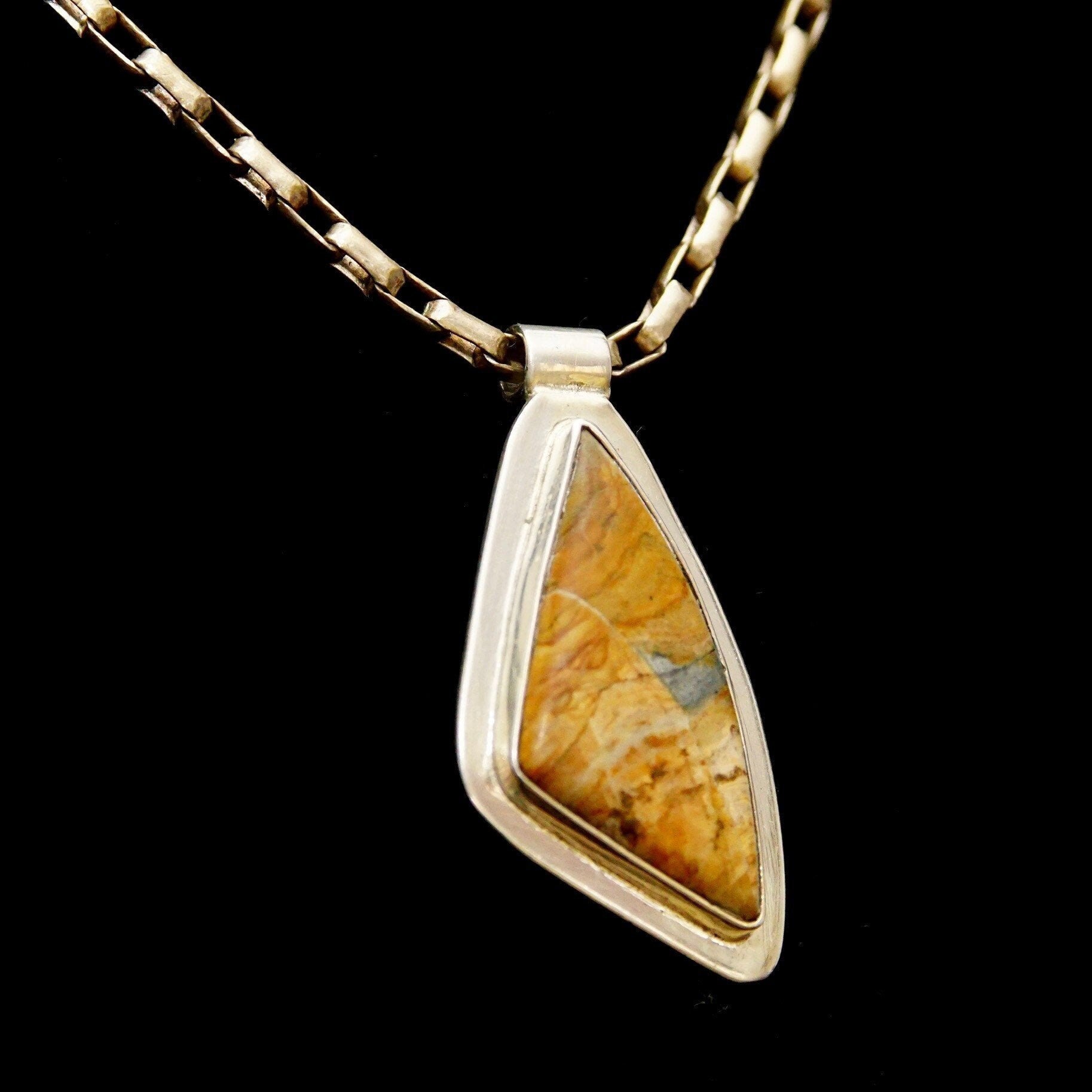 Alt text: Vintage modernist sterling silver pendant with abstract triangular bezel setting featuring fossilized gemstone, on gold tube link chain against black background