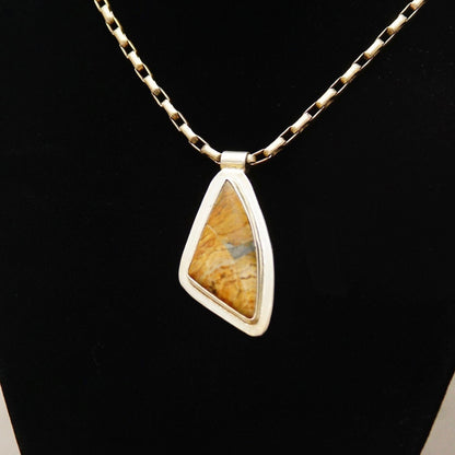 Vintage modernist sterling silver pendant necklace with abstract triangular bezel-set yellow gemstone or fossil, hung from a delicate chain, against a black background.