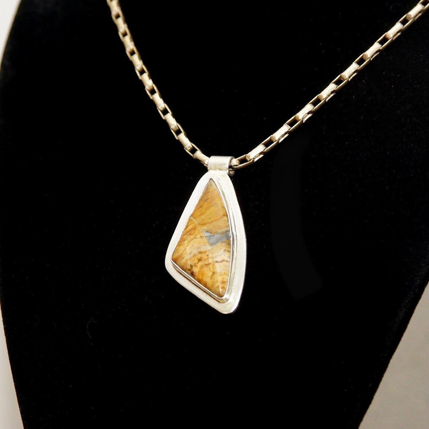 Vintage modernist sterling silver pendant necklace with abstract triangular bezel-set yellow gemstone or fossil, on gold chain against black background