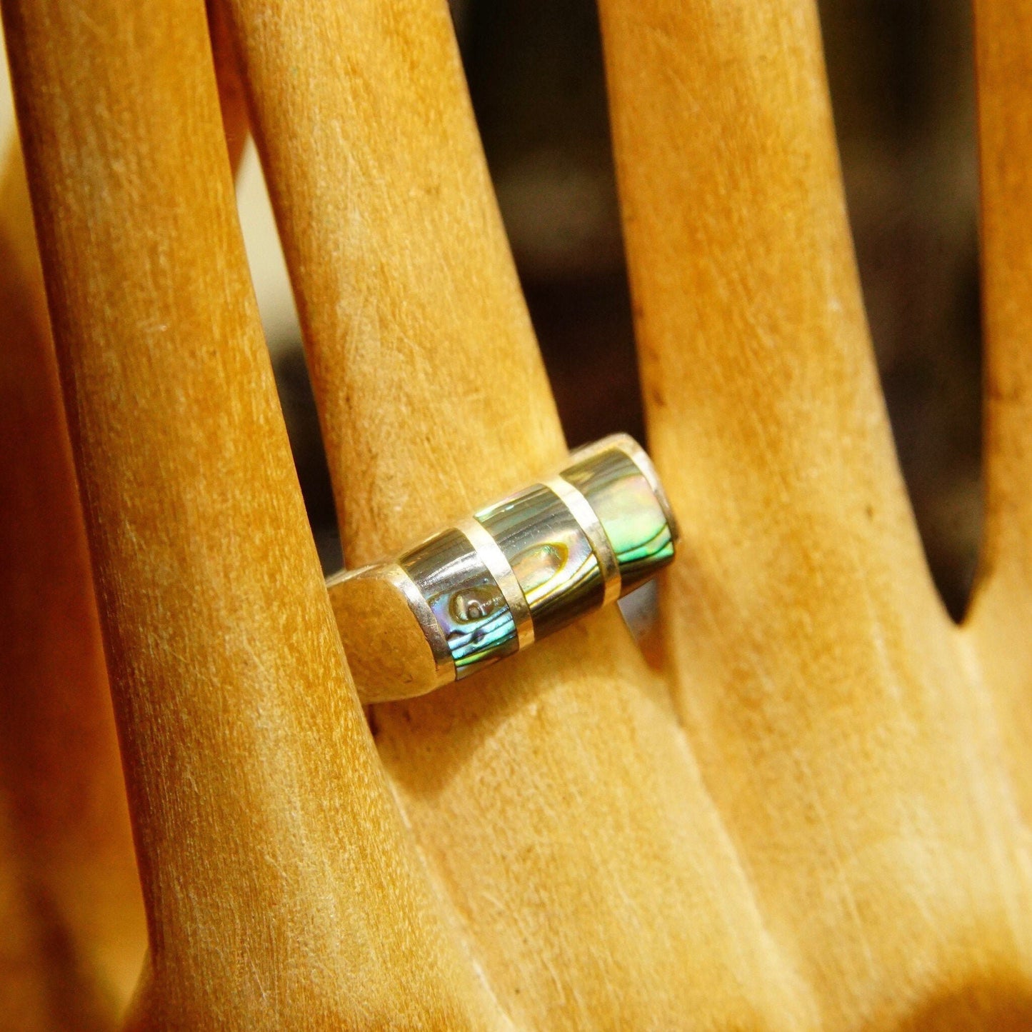 Alt text: Close-up view of two sterling silver rings with abalone inlay resting on wooden dowels