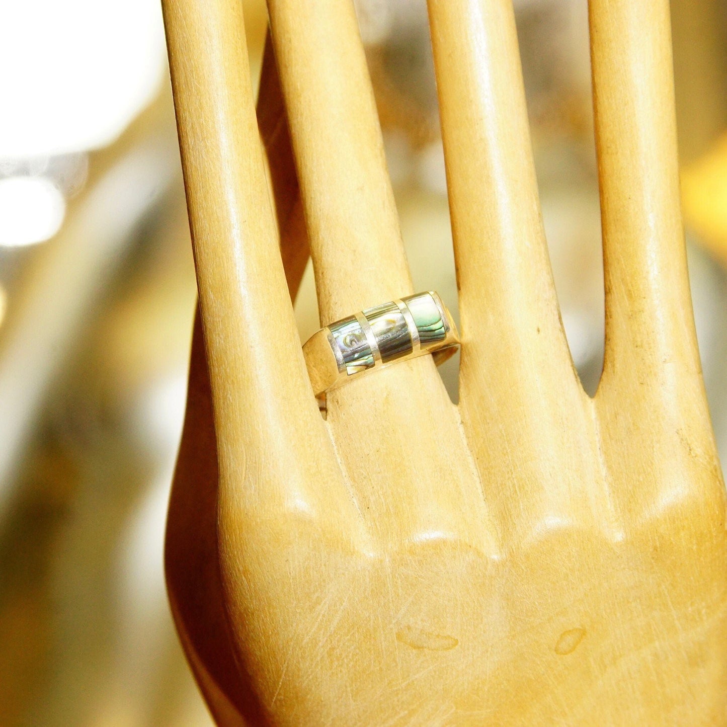 Vintage sterling silver saddle ring with abalone inlay on wooden hand mannequin, closeup view