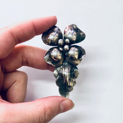 Vintage silver flower brooch pin with dark patina from John Wanamaker, held between fingers to display intricate leaf design and craftsmanship of the unique 925 silver jewelry piece.