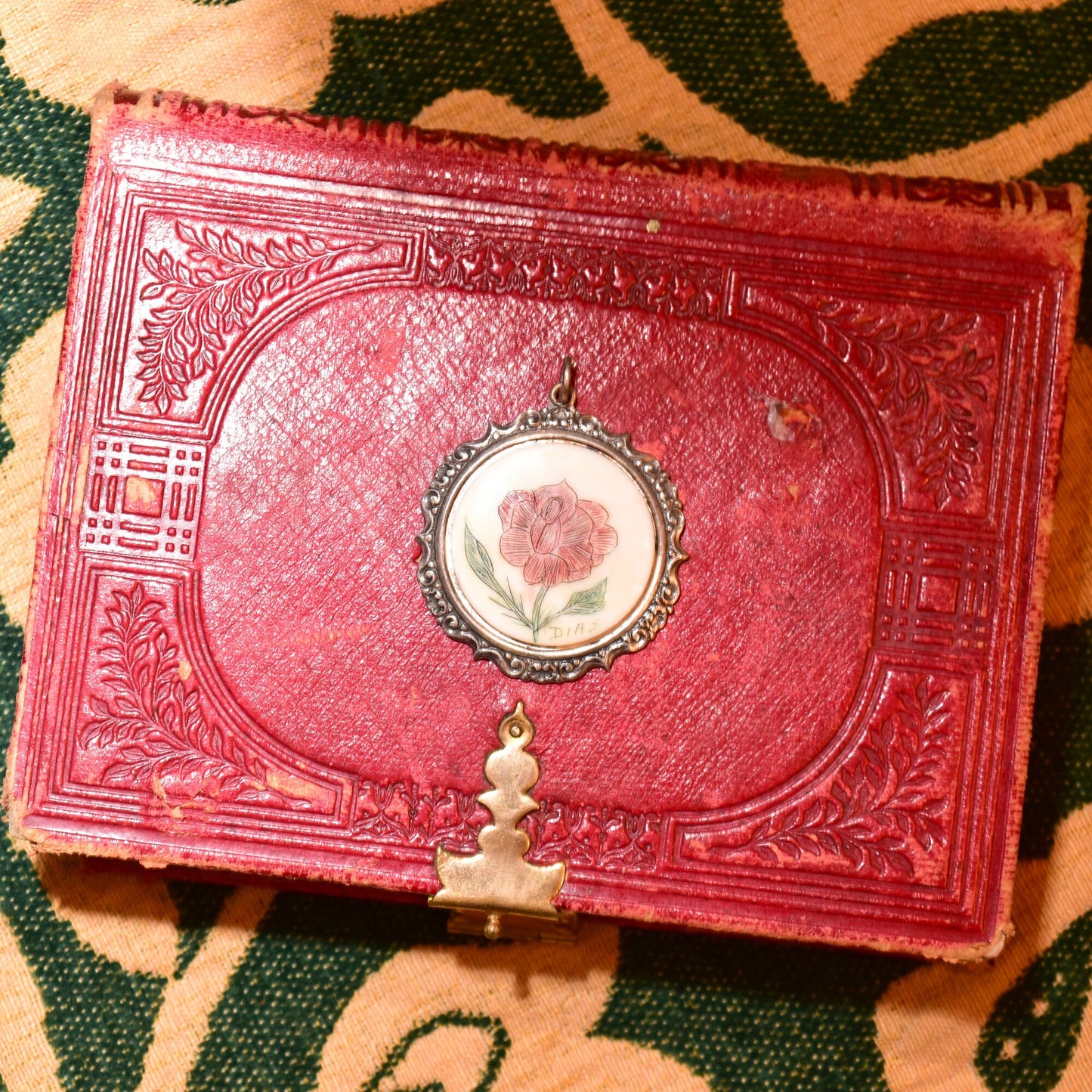 Signed scrimshaw flower pendant in sterling silver hand-etched and inked on bovine bone, set in antique red leather repousse book cover