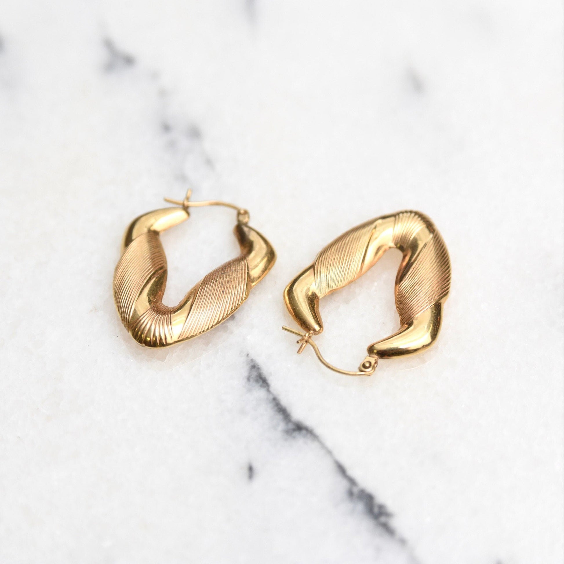 14K yellow gold textured puffed V-shaped hoop earrings with hinged ear wires, small to medium size, 1 3/8 inches long, on white marble background