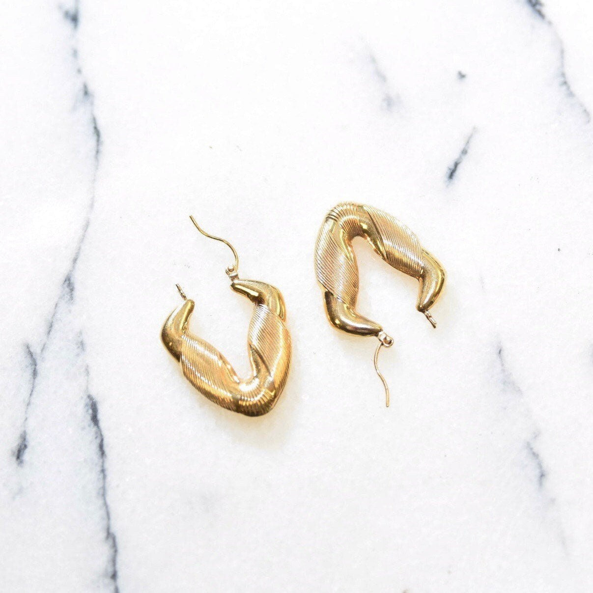 14K yellow gold textured chevron hoop earrings on marble background