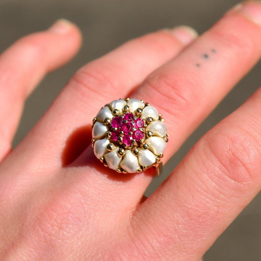 14K yellow gold estate ring featuring a cluster of white pearls surrounding a pink ruby center stone in a floral dome bombe design, shown on a hand, size 9 US.